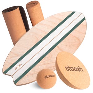 Può includere: Una collezione di attrezzature per il fitness in sughero, tra cui una balance board a forma di tavola da surf con strisce verdi e bianche, un tappetino arrotolato, un rullo cilindrico, una palla e un blocco ovale. Il marchio "staash" è stampato.