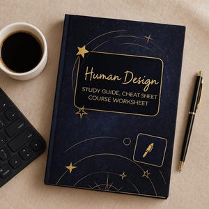 Op de afbeelding: Een marineblauw boek met de titel "Human Design" in gouden letters en sterren. Een zwarte pen met gouden details, een kopje koffie en een zwart toetsenbord zijn ook zichtbaar.