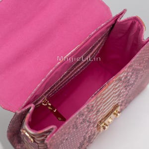 May include: Pink handbag with a snakeskin pattern. The bag is open, revealing a bright pink interior and a zippered pocket. Gold-colored hardware accents the bag's closure and strap attachments. The text "MagicLilin" is visible inside the bag.