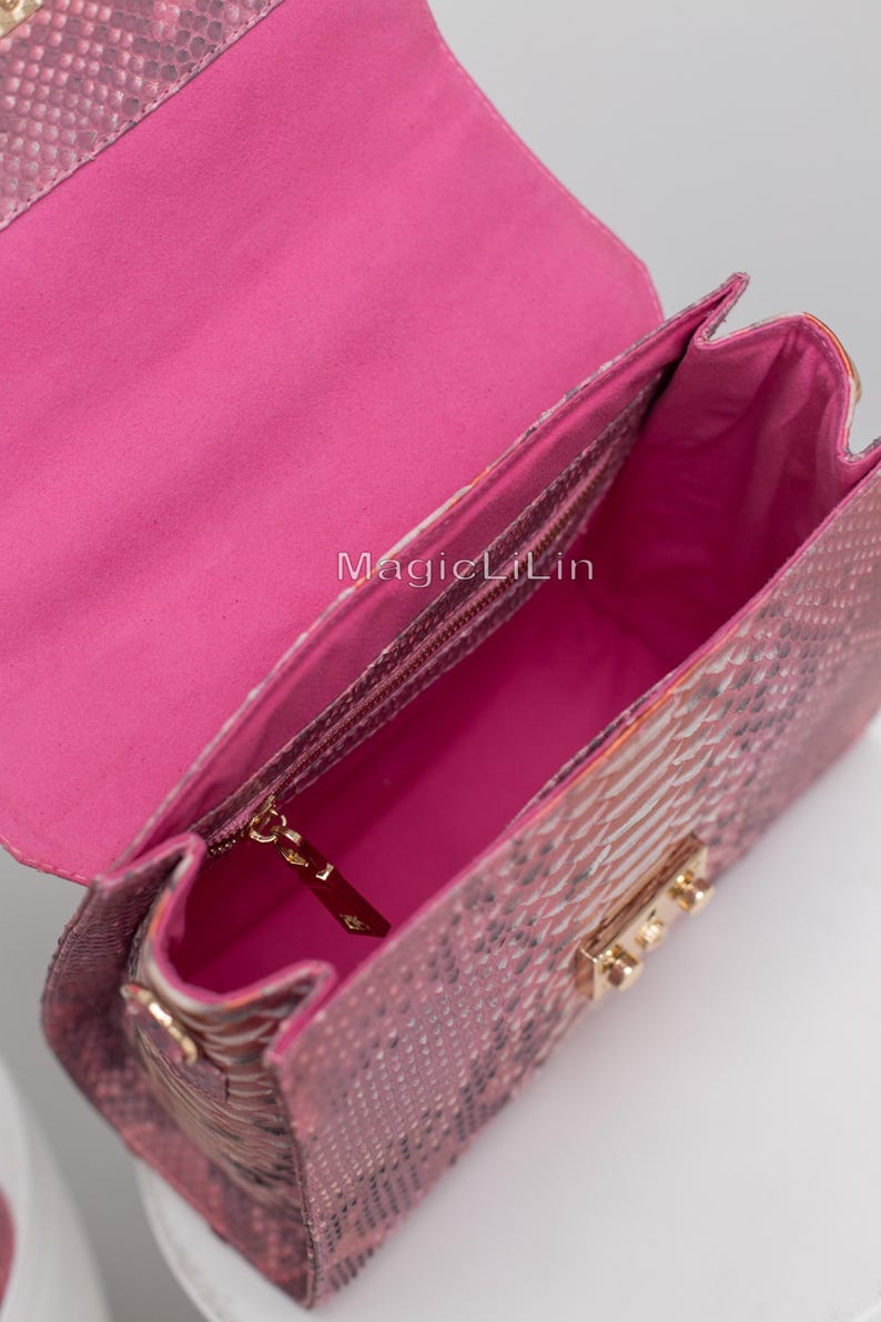 May include: Pink handbag with a snakeskin pattern. The bag is open, revealing a bright pink interior and a zippered pocket. Gold-colored hardware accents the bag's closure and strap attachments. The text "MagicLilin" is visible inside the bag.