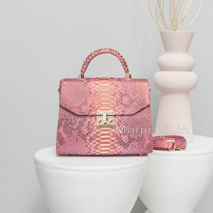 Peut inclure: Sac à main en peau de serpent rose et orange avec une poignée supérieure et un fermoir doré. Une bandoulière assortie est à côté du sac. Le sac est sur une table blanche. Le texte "MagicLiLin" est sur le sac.