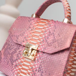 May include: Pink and orange snakeskin handbag with a top handle and gold-colored hardware. The bag has a flap closure with a gold-colored clasp. The text "MagicLili" is visible on the front of the bag.