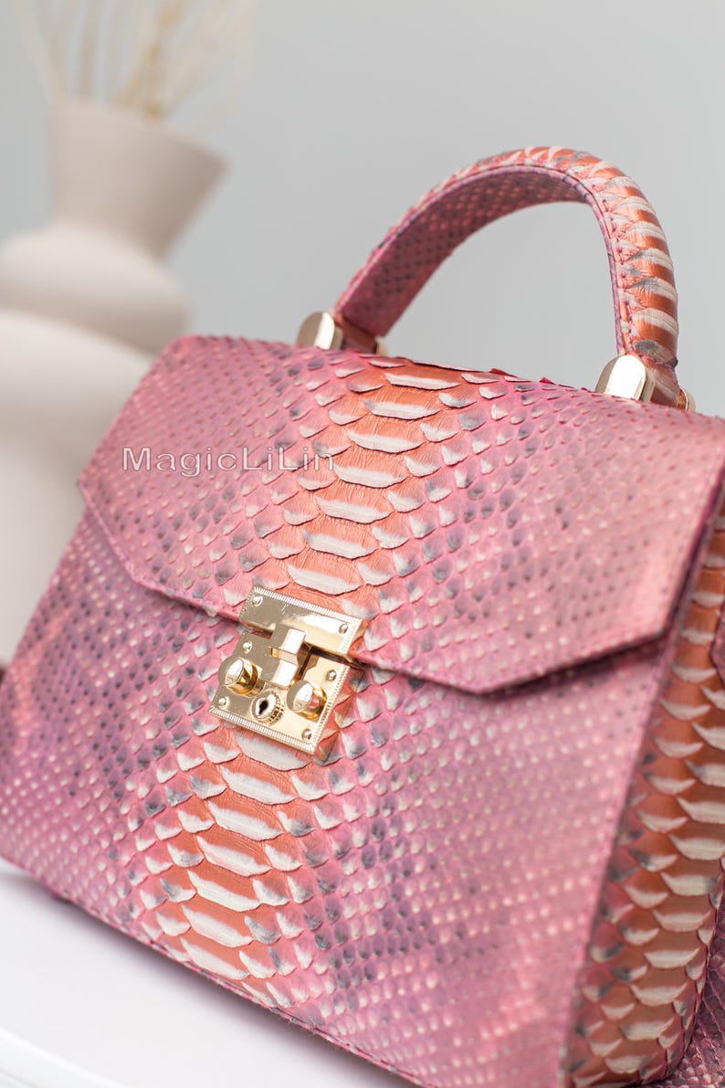 May include: Pink and orange snakeskin handbag with a top handle and gold-colored hardware. The bag has a flap closure with a gold-colored clasp. The text "MagicLili" is visible on the front of the bag.