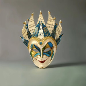 May include: A white and blue Venetian masquerade mask with a jester's hat. The hat is decorated with musical notes and gold accents. The mask has a smiling face with blue and gold accents.