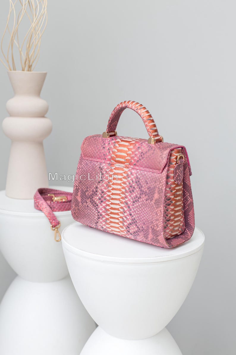 May include: Pink handbag with a snakeskin pattern, featuring a top handle and a detachable shoulder strap. The bag has gold-colored hardware and is displayed on a white surface. The text "MagicLilin" is visible on the side of the bag.