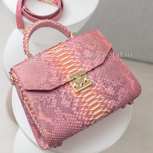 May include: Pink snakeskin handbag with a top handle and a detachable shoulder strap. The bag features a gold-tone clasp and hardware. The text "MagicLiLin" is visible on the bag.