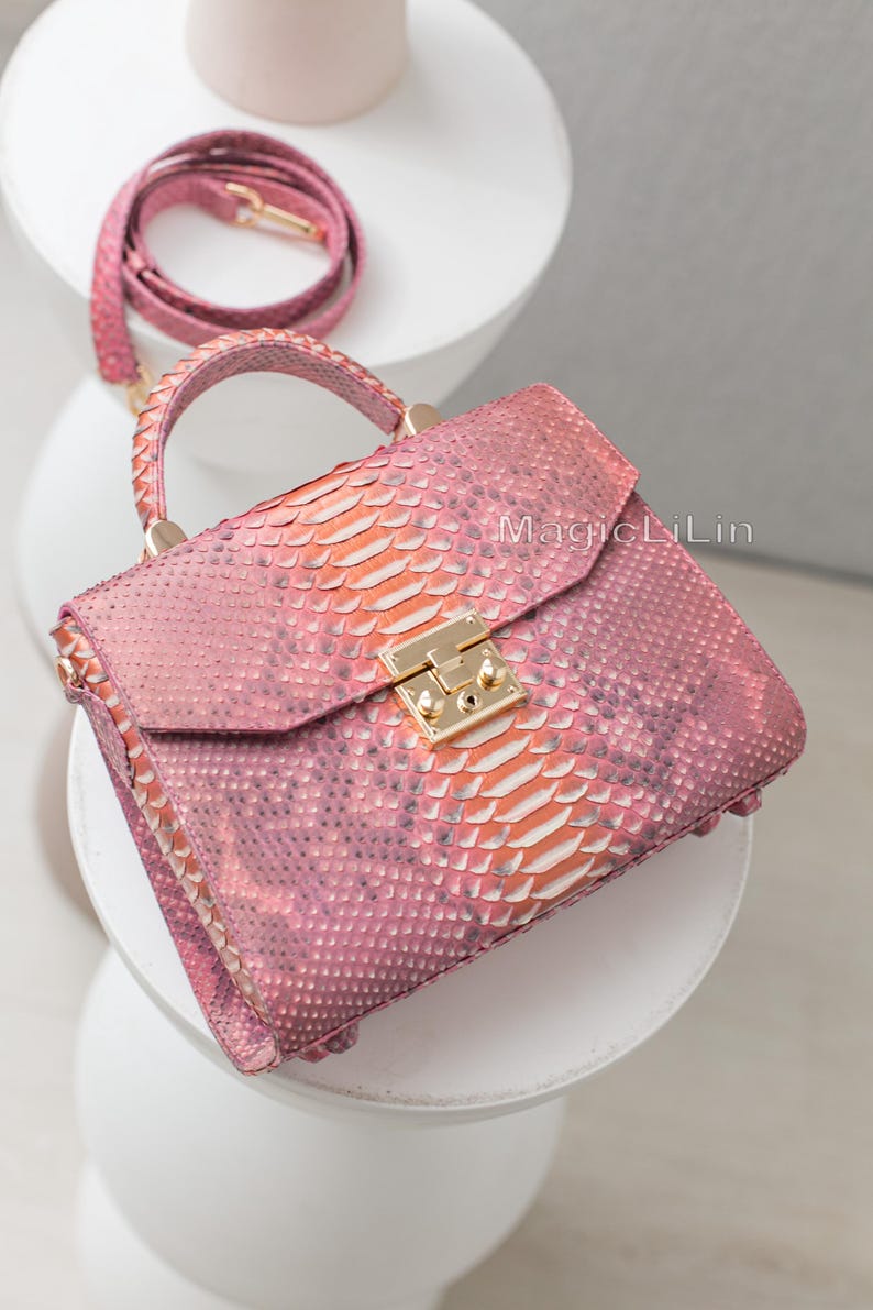 May include: Pink snakeskin handbag with a top handle and a detachable shoulder strap. The bag features a gold-tone clasp and hardware. The text "MagicLiLin" is visible on the bag.