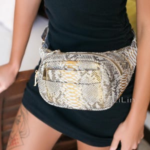 Könnte beinhalten: Eine Bauchtasche mit Schlangenmuster und goldenem Reißverschluss und Akzenten. Die Tasche hat eine Vordertasche und ein Hauptfach. Der Text "Magic LiLin" ist sichtbar. Die Tasche wird um die Taille getragen.