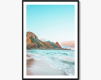 May include: A framed vertical wall art print featuring a coastal landscape with a sandy beach, turquoise ocean waves, and rugged mountains under a clear blue sky. The mountain peaks are illuminated by soft golden light, and clouds are visible.