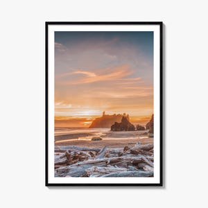 May include: A framed vertical wall art print featuring a coastal landscape at sunset. The foreground is filled with weathered driftwood on a sandy beach, leading to dark rock formations in the ocean under a vibrant orange and blue sky.