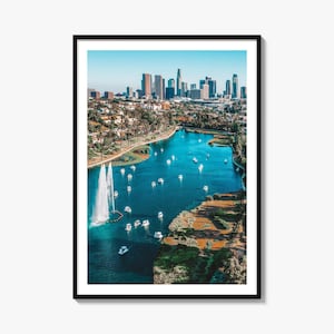 May include: A framed wall art print featuring an aerial view of Echo Park Lake in Los Angeles. The scene displays a vibrant blue lake with numerous white pedal boats, a tall water fountain, and the distant city skyline under a clear sky.