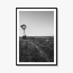Könnte beinhalten: Ein schwarz-weiß gerahmter Kunstdruck, der eine ländliche Landschaft mit einer hohen Windmühle aus Metall auf einem grasbewachsenen Feld unter klarem Himmel zeigt. Die Szene zeigt eine weite Fläche mit einer markanten Windpumpenstruktur.