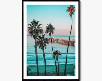 May include: A framed wall art print featuring a coastal scene with four tall palm trees in the foreground. The background shows a long wooden pier extending into the calm ocean under a clear sky that transitions from light blue to soft pink.