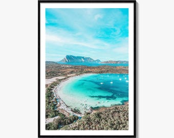 May include: A framed vertical wall art print featuring an aerial view of a turquoise coastal bay with white sand beaches, scattered small boats, and dense green vegetation, set against a distant mountain range under a bright blue sky.