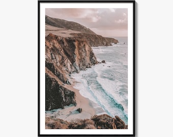 May include: A framed wall art print featuring a coastal landscape with rugged brown cliffs meeting the ocean. White waves crash against the sandy shore under a soft, hazy sky. The scene captures a high-angle view of the coastline with earthy tones.