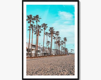 Pode incluir: Uma impressão de arte de parede emoldurada apresentando uma praia de areia em primeiro plano com uma fileira de palmeiras altas que se estendem ao longe. Atrás das árvores, edifícios residenciais de vários andares sob um céu azul ciano.