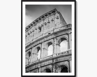 May include: A black and white framed wall art print featuring a low-angle view of the Colosseum in Rome. The image captures the ancient stone structure with its iconic tiered arches, weathered masonry, and columns against a cloudy sky.