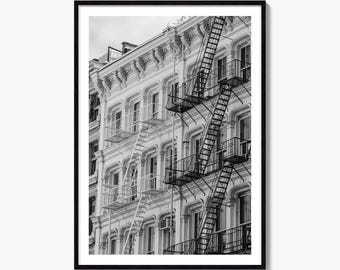 May include: A black and white architectural photograph of a multi-storey building facade featuring ornate cornices, multiple windows, and prominent black metal fire escape staircases attached to the exterior wall, all framed within a thin black border.