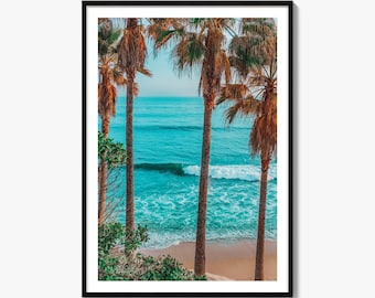 May include: A framed wall art print featuring a vertical view of a turquoise ocean with gentle white-capped waves rolling onto a sandy beach, framed by tall, slender palm trees with brown trunks and green fronds under a clear blue sky.