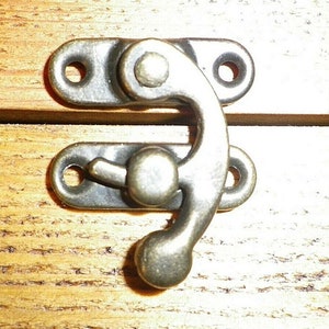 May include: Antique brass latch with a rounded handle and two holes for mounting. The latch is designed to be used on a wooden box or chest.