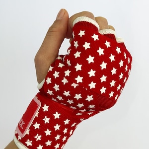 May include: Red boxing hand wraps with white stars. The wraps have a white trim and a red patch with the word "MX" on it.