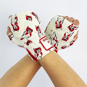 May include: White boxing hand wraps with a red and black cat print. The wraps have a red label that says "RAIX" on it.