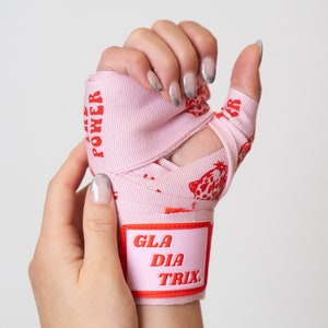 Könnte beinhalten: Rosa Hand Wraps mit einem roten Leopardenmuster und dem Text "GLADIA TRIX" auf einem rosa Patch. Der Text "GIRL POWER" ist auf dem Wrap gedruckt.