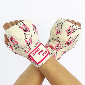May include: A pair of white hand wraps with a pink cat print and a pink label that says "GLA DIA TRIX".