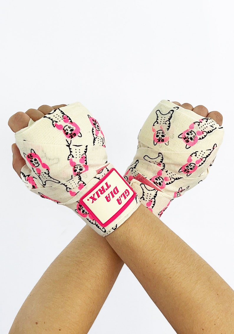 May include: A pair of white hand wraps with a pink cat print and a pink label that says "GLA DIA TRIX".