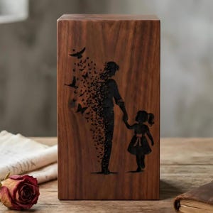 Puede incluir: Una urna rectangular de madera con veteado marrón oscuro. La superficie frontal presenta una silueta negra grabada con láser de un adulto y un niño tomados de la mano, con la figura del adulto disolviéndose en una bandada de aves pequeñas.