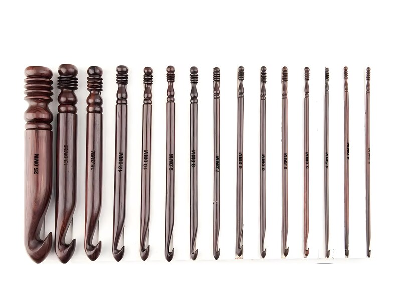 May include: A set of fifteen dark brown wooden crochet hooks arranged in descending order of size. Each hook features a grooved handle and is clearly marked with its specific metric size, ranging from 25.0mm down to 3.0mm, printed on the shaft.