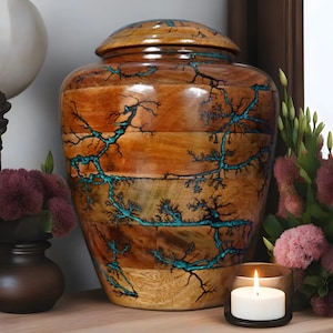 May include: A wooden urn with a teal blue lightning bolt design. The urn has a lid and is made of wood.