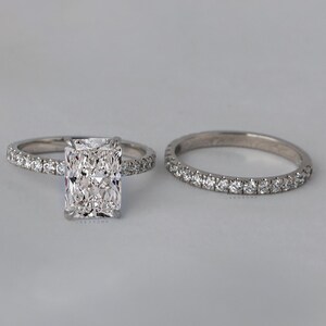 May include: A set of two diamond engagement rings. The main ring features a large, rectangular-shaped diamond with smaller diamonds set in a band. The second ring is a simple band with small diamonds set in a pave setting.