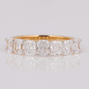 Op de afbeelding: Een gouden band met een rij van zeven kussen geslepen diamanten. De diamanten zijn gezet in een pavé setting en zijn omgeven door kleinere diamanten.