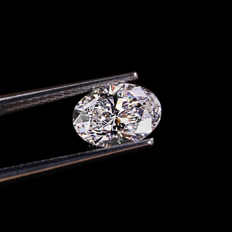 May include: A sparkling, oval-cut diamond held by silver tweezers against a black background. The diamond's facets reflect light, creating a brilliant display of color and sparkle. The image highlights the clarity and cut of the gemstone.