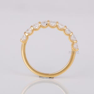May include: A gold ring with a series of clear, oval gemstones. The ring has a polished band and the gemstones are set closely together. The ring is shown against a white backdrop. The text "AKSHAR LABGROWN" is visible on the ring.