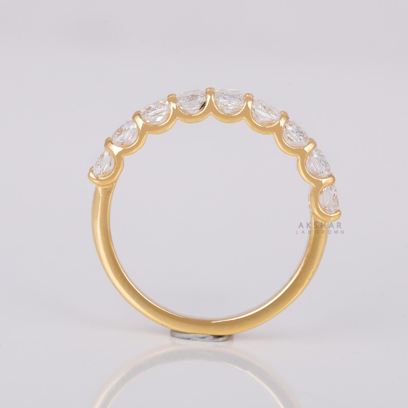 May include: A gold ring with a series of clear, oval gemstones. The ring has a polished band and the gemstones are set closely together. The ring is shown against a white backdrop. The text "AKSHAR LABGROWN" is visible on the ring.