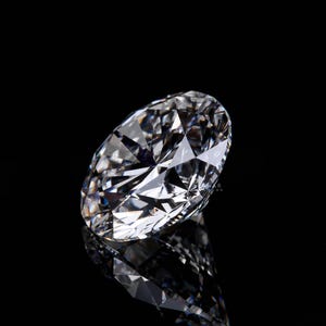 May include: A large, clear diamond with many facets, reflecting light and creating a brilliant sparkle. The diamond is set against a black background, with its reflection visible below. The gemstone is a symbol of luxury and elegance.
