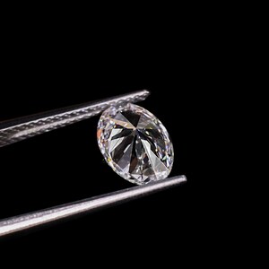 May include: A brilliant, oval-cut diamond held by silver tweezers against a black background. The diamond's facets reflect light, creating a sparkling effect. The image highlights the clarity and brilliance of the gemstone.
