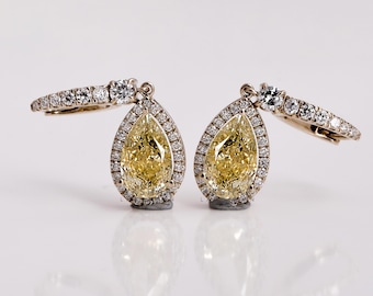 May include: A pair of gold earrings featuring pear-shaped yellow diamonds set in a halo of smaller diamonds.