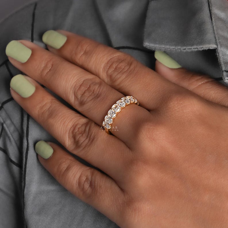 May include: A gold ring set with multiple clear gemstones. The ring features a series of round-cut stones, forming a continuous band of sparkle. The ring is on a hand with light green nail polish.