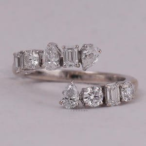 Può includere: Un anello d'argento con un design unico che presenta più diamanti di diverse forme e dimensioni. L'anello è incastonato con un diamante a forma di pera, un diamante rotondo e diversi diamanti baguette.