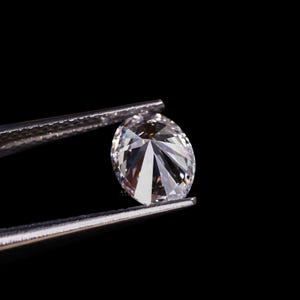 May include: A brilliant, oval-cut diamond held by silver tweezers against a black background. The diamond's facets reflect light, creating a sparkling effect. The image highlights the clarity and brilliance of the gemstone.
