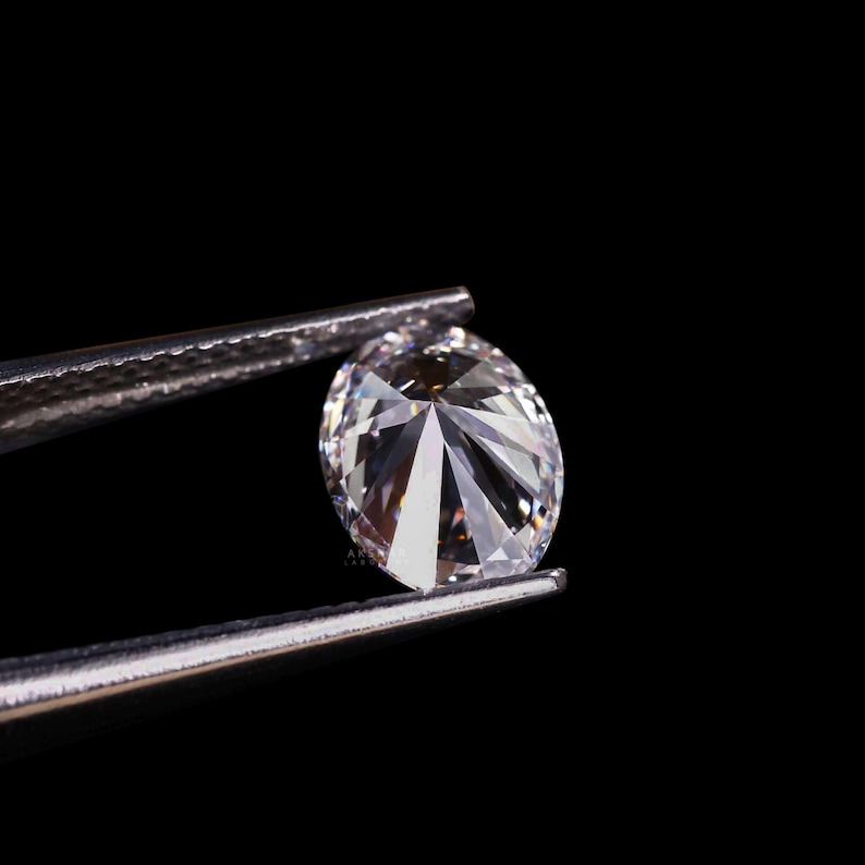 May include: A brilliant, oval-cut diamond held by silver tweezers against a black background. The diamond's facets reflect light, creating a sparkling effect. The image highlights the clarity and brilliance of the gemstone.
