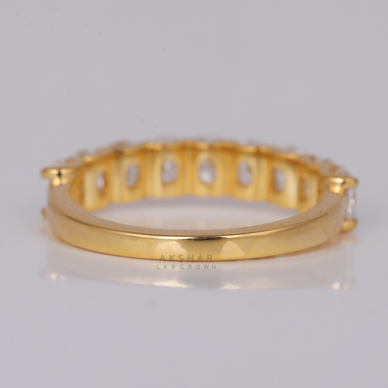 May include: A gold ring featuring a line of clear, oval-cut gemstones. The ring has a polished finish, and the text "AKSHAR LAB GROWN" is visible on the band.