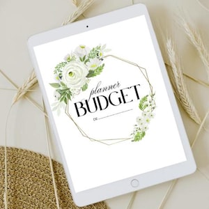 Könnte beinhalten: Ein weißes Tablet zeigt ein Blumendesign mit den Worten "planner BUDGET" in Schwarz. Das Design umfasst weiße Rosen und Grün innerhalb eines goldenen geometrischen Rahmens. Das Tablet ist von Weizenähren und einer gewebten Matte umgeben.