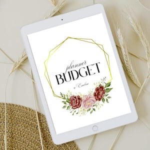 Peut inclure: Une tablette blanche affiche un design floral avec les mots "planner BUDGET" en noir, encadrés par une forme géométrique dorée. Le design comprend des fleurs bordeaux et roses. La tablette est entourée d'épis de blé et d'un tapis tissé.