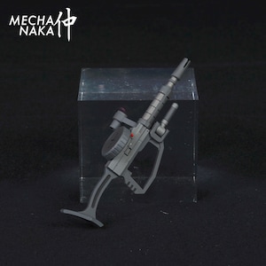 May include: A gray plastic toy gun with a black handle and a red button. The gun has a barrel with a black and silver design. The gun is on a clear acrylic display stand.