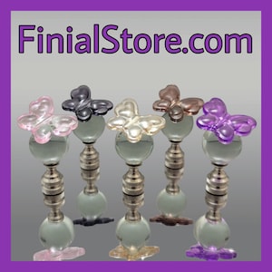 May include: Five glass finials with butterfly designs in pink, purple, black, brown, and white. The finials are attached to a silver metal base.