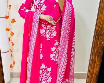 May include: A vibrant pink ensemble featuring a long-sleeved tunic, matching pants, and a flowing scarf. The outfit is adorned with a white floral pattern. The scarf and the edges of the pants have a decorative border. The outfit is made of a lightweight fabric.